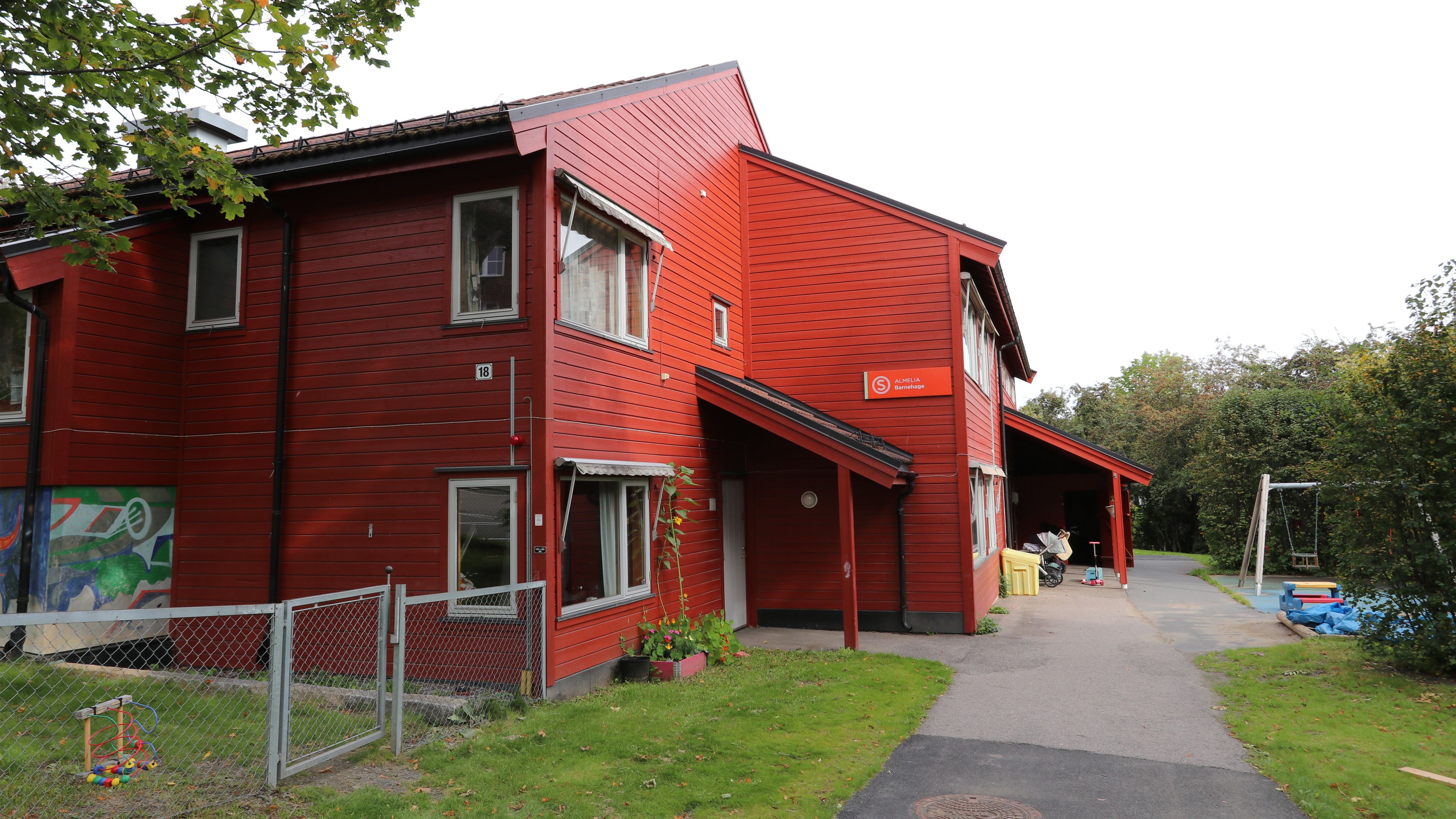 Et bilde av Almelia barnehage. Et rødt hus med lekeplass rundt.
