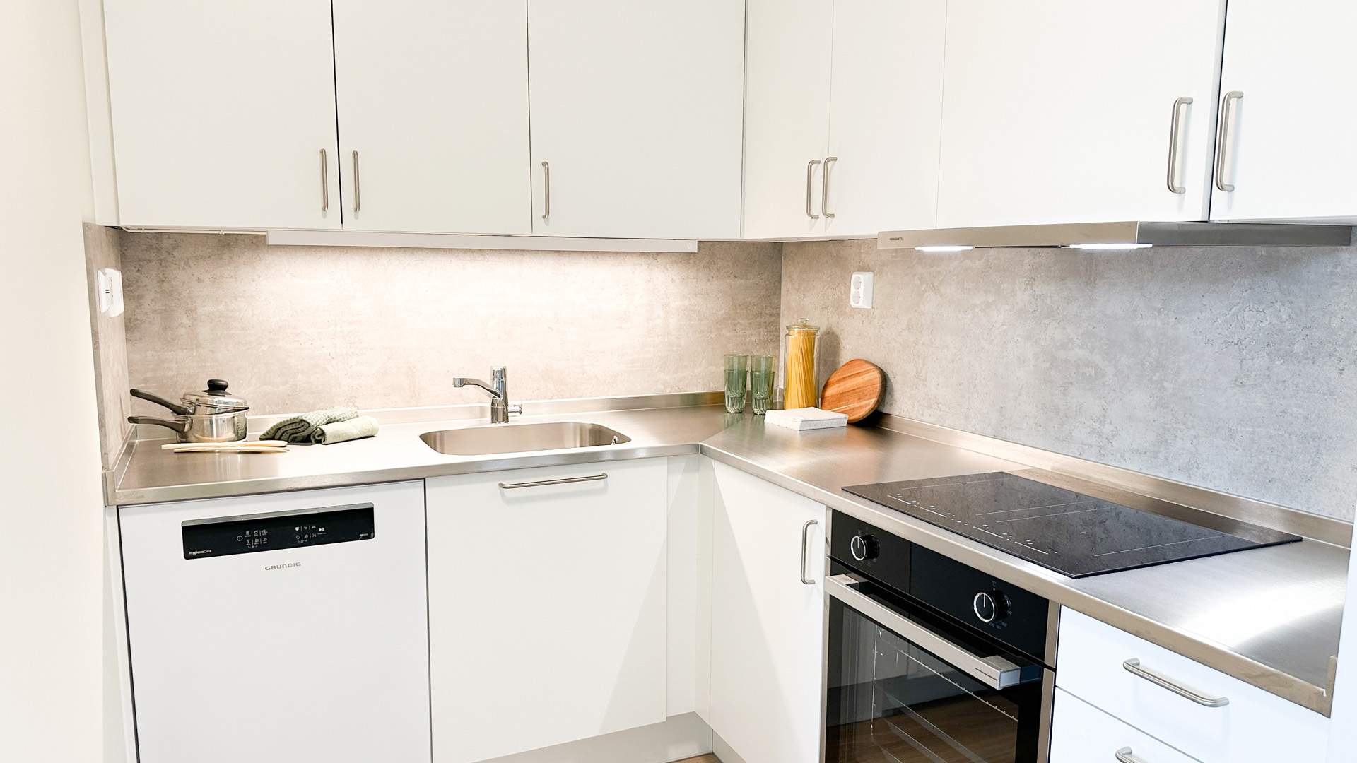 Foto av kjøkken med hvite flater og benkeplate i stål.